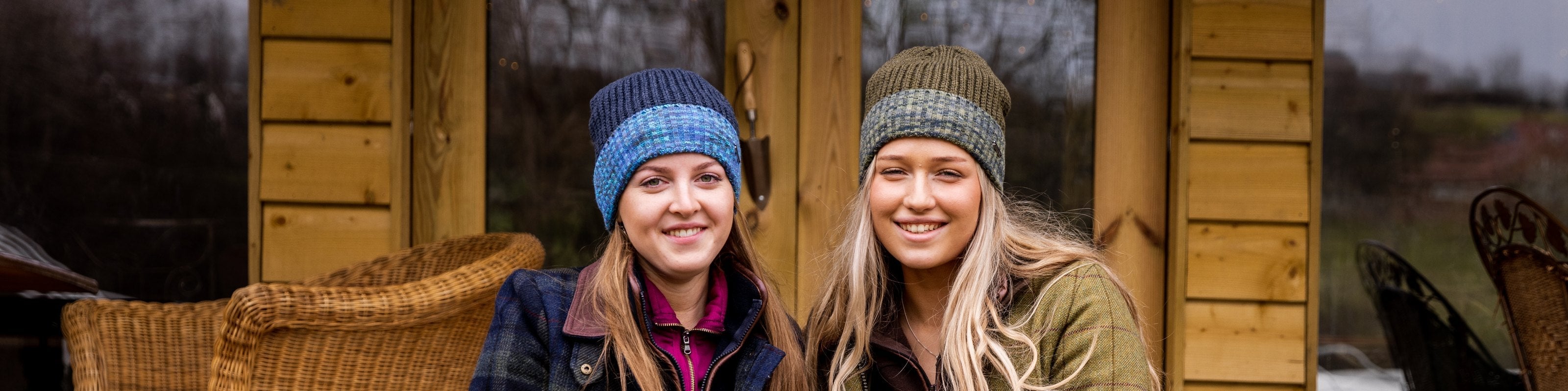 Two women sitting on wooden cabin steps, smiling, wearing SABBOT Morgan beanies in Blue Camo and Green Camo