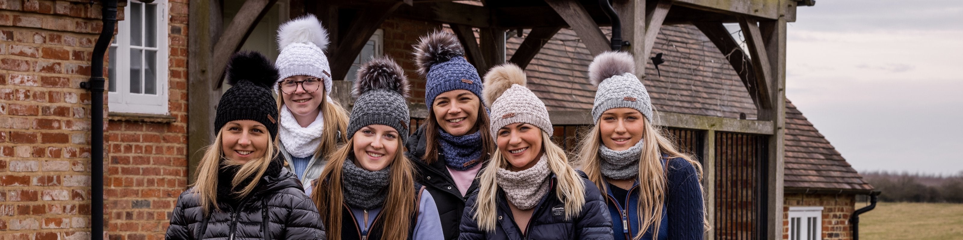 Six friends by a brick barn wearing SABBOT bobble hats and matching snoods