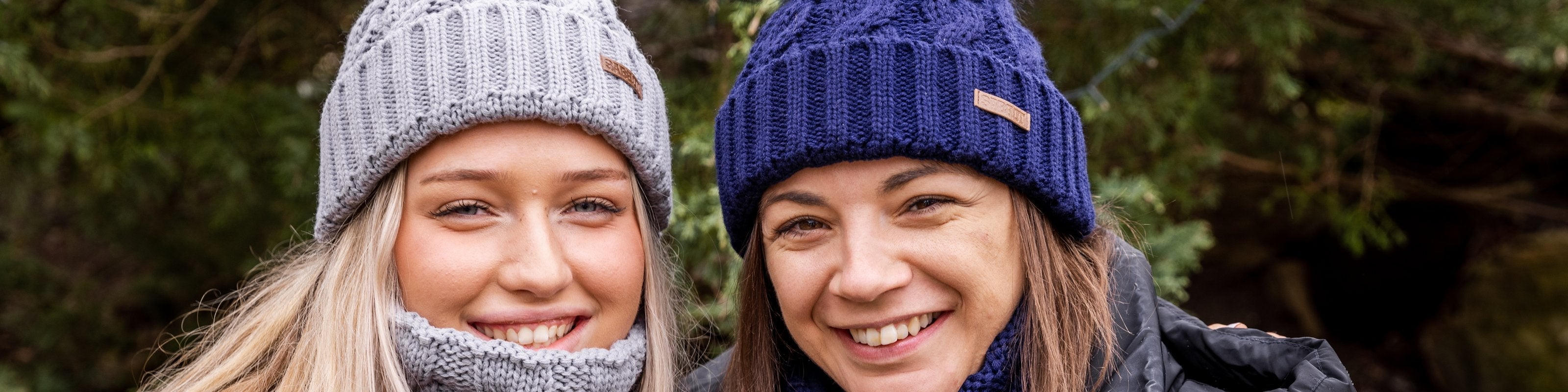 Two smiling friends in SABBOT light grey and navy cable-knit hats with matching snoods