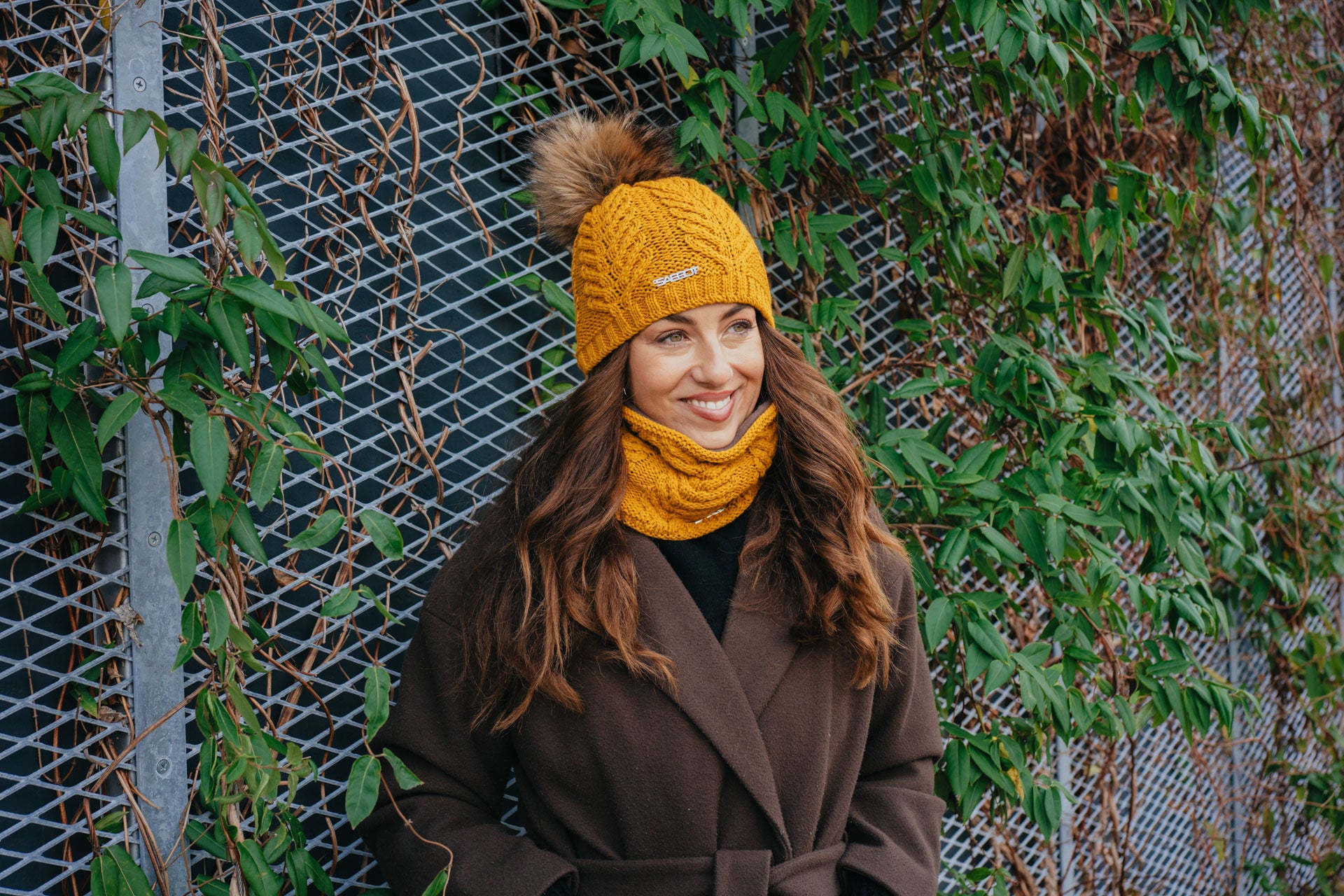 Sabbot Headwear Woman wearing matching Emma mustard knitted bobble hat and snood