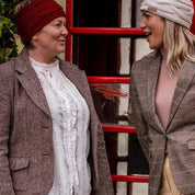 Two friends in tweed jackets chatting by a red phone box wearing SABBOT Linda cable knit headbands in Burgundy and Cream
