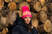 Sabbot Headwear Lady wearing a neon pink SABBOT beanie at a ski resort Sabbot Headwear