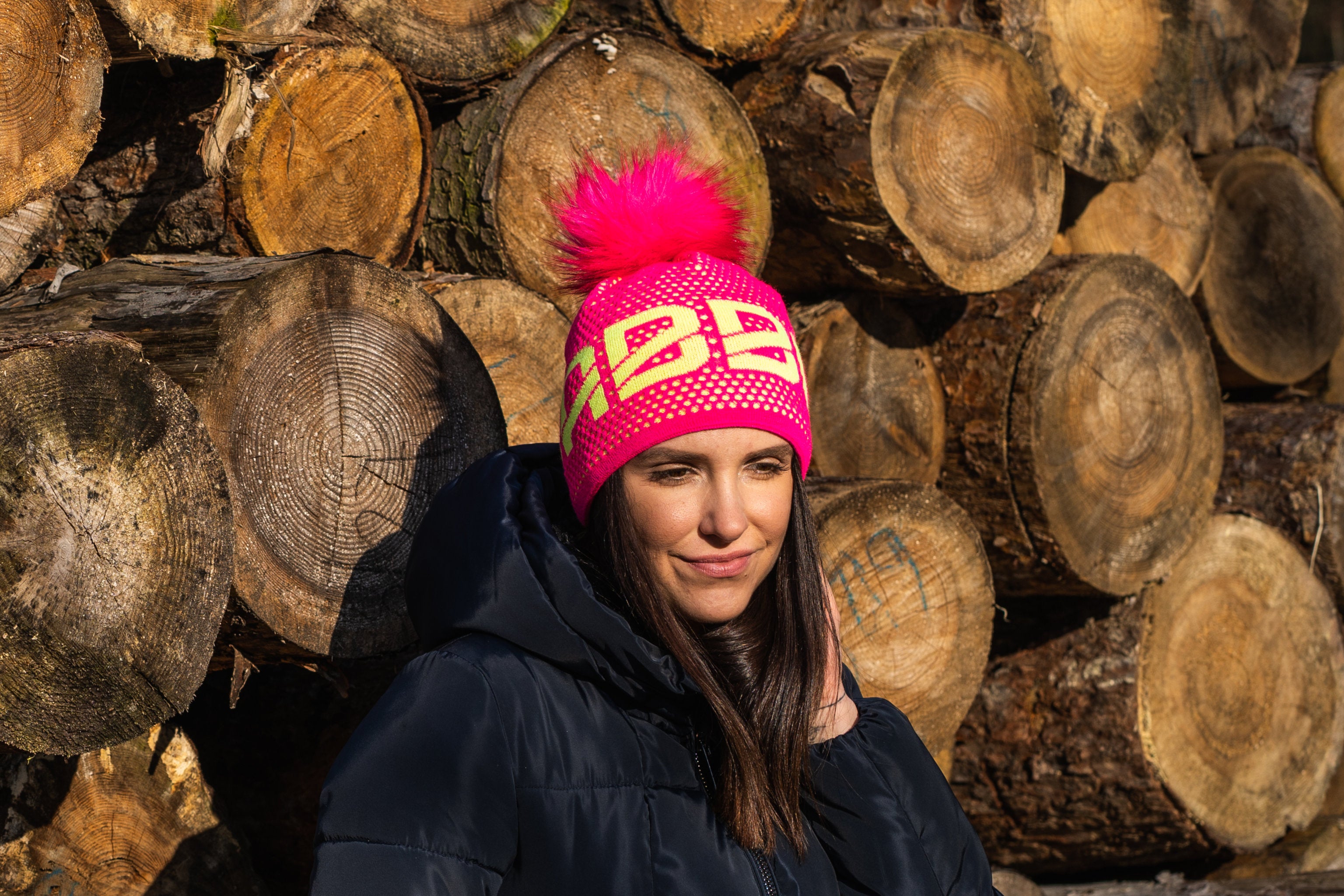 Sabbot Headwear Lady wearing a neon pink SABBOT beanie at a ski resort Sabbot Headwear
