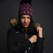 A woman in a black ski jacket wearing the SABBOT Alice tartan bobble hat in Pink/Black