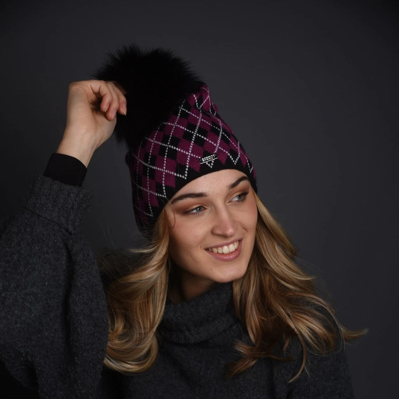 A woman wearing the SABBOT Alice Bobble Hat in Pink/Black with a black faux fur pom pom