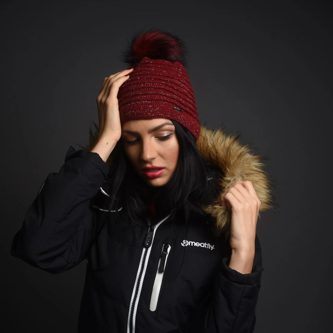 A woman in a black ski jacket wearing the SABBOT Blanka Bobble Hat in Burgundy