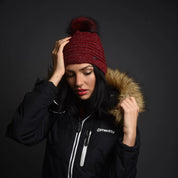 A woman in a black ski jacket wearing the SABBOT Blanka Bobble Hat in Burgundy