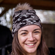 A smiling woman under a barn roof wearing the Calli Bobble Hat in Brown Camo