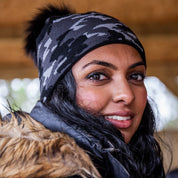 A smiling woman under a barn roof wearing the Calli Bobble Hat in Grey Camo