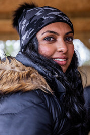 A smiling woman under a barn roof wearing the Calli Bobble Hat in Grey Camo