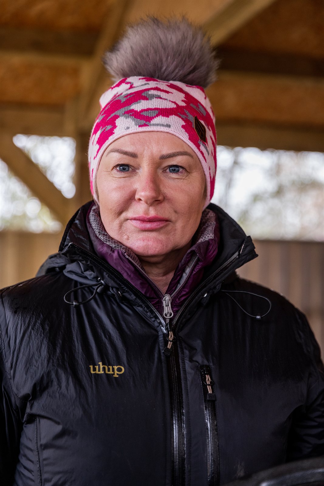 A smiling woman under a barn roof wearing the Calli Bobble Hat in Pink Camo