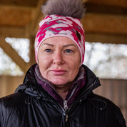 A smiling woman under a barn roof wearing the Calli Bobble Hat in Pink Camo
