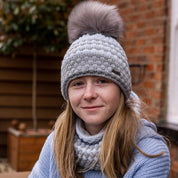 A teenager sitting on a garden bench wearing the Chloe Bobble Hat and Snood in Grey/White