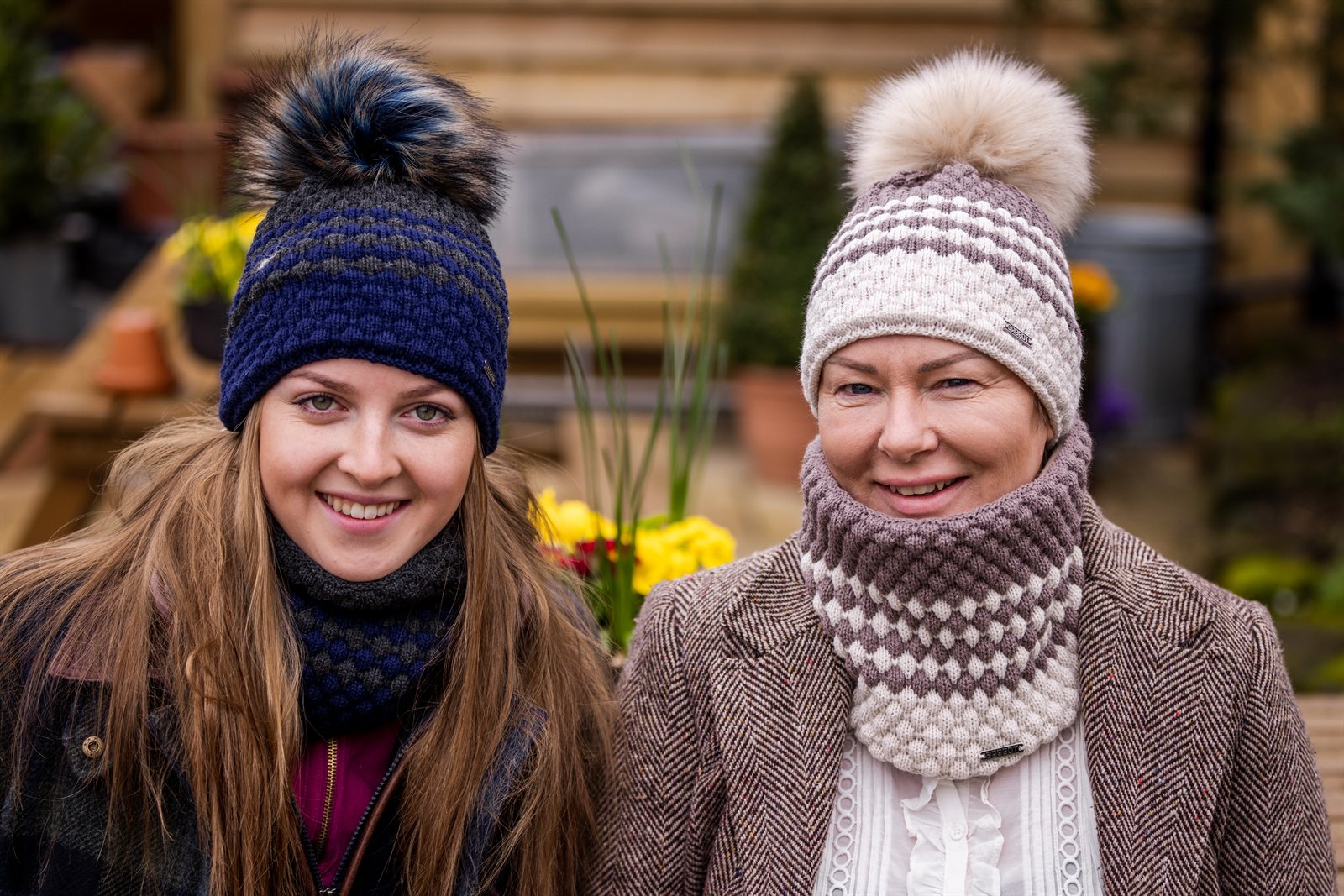 Two women in matching hat and snood sets wearing the Chloe Bobble Hats and Snoods in Navy/Pink and Brown/Cream