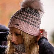 A woman adjusting her pink and grey bubble-knit hat wearing the Chloe Bobble Hat and Snood in Pink/Grey