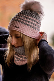 A woman adjusting her pink and grey bubble-knit hat wearing the Chloe Bobble Hat and Snood in Pink/Grey
