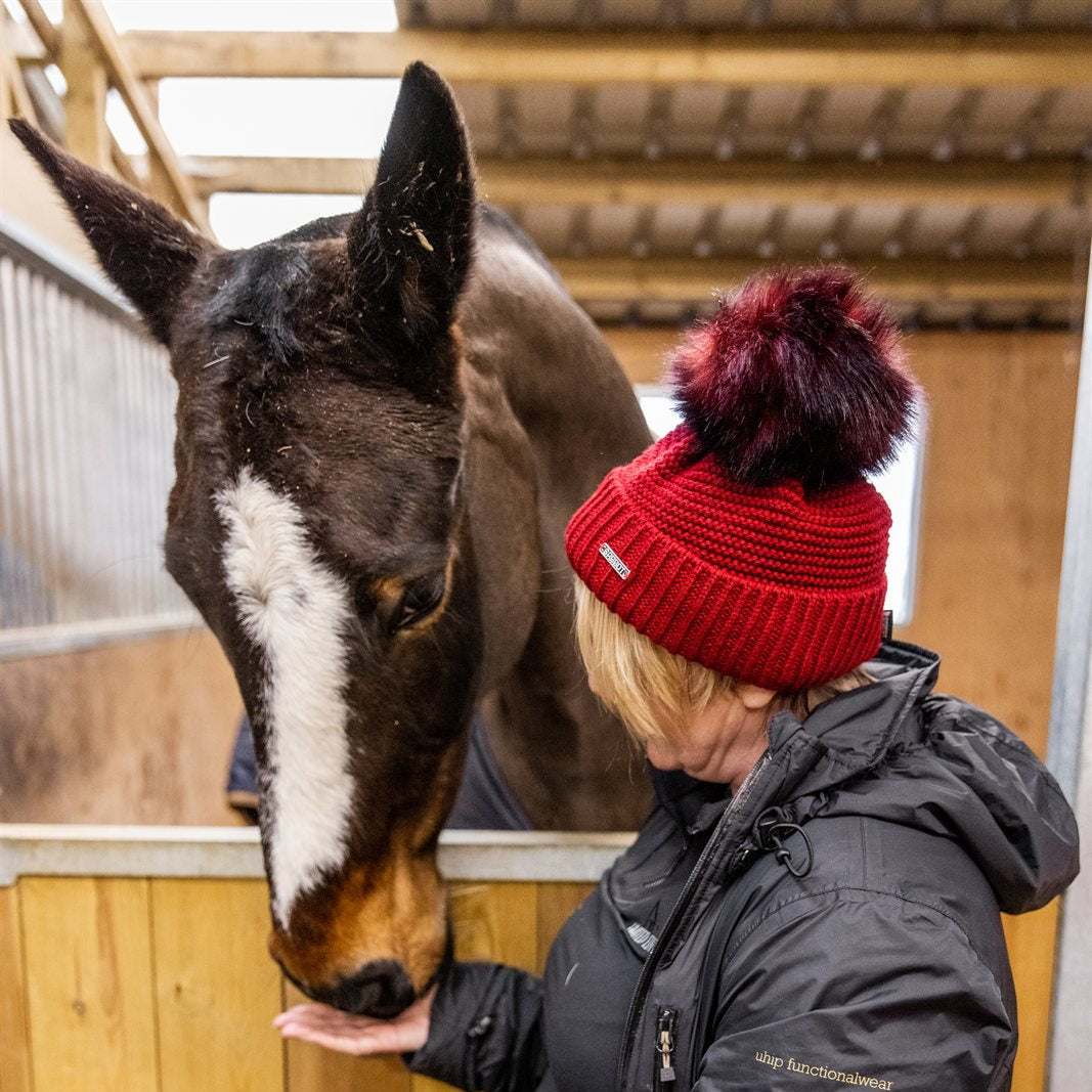 A woman with a horse in the stables wearing the Eva Bobble Hat in Burgundy