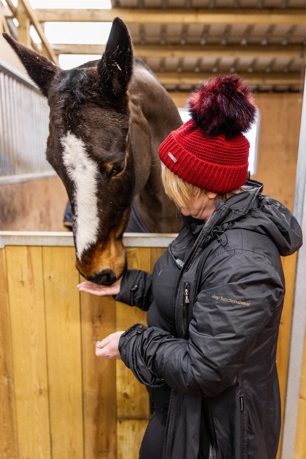 A woman with a horse in the stables wearing the Eva Bobble Hat in Burgundy