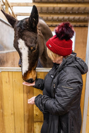 A woman with a horse in the stables wearing the Eva Bobble Hat in Burgundy