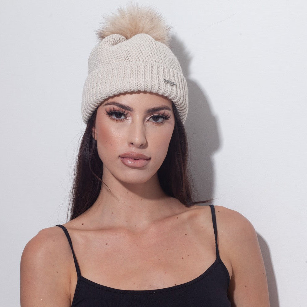 Woman wearing the SABBOT Eva knitted bobble hat in cream with faux fur pom pom