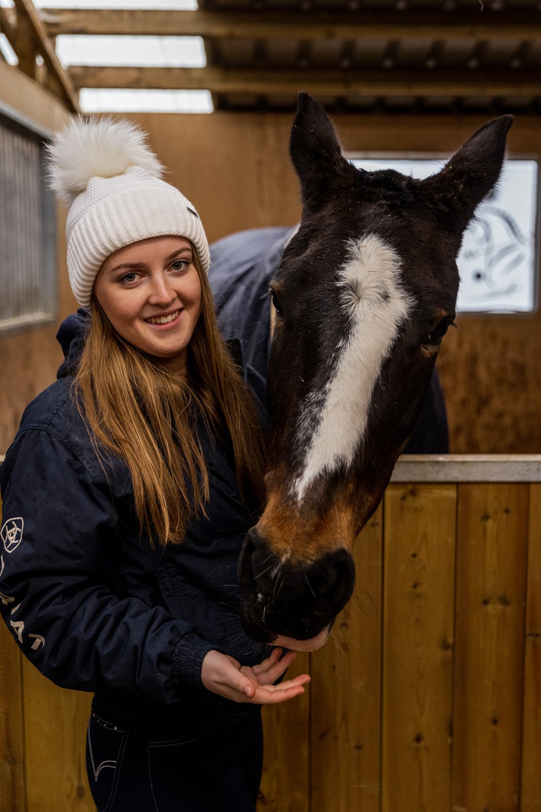 A woman with a horse in the stables wearing the Eva Bobble Hat in Cream