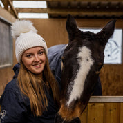 A woman with a horse in the stables wearing the Eva Bobble Hat in Cream
