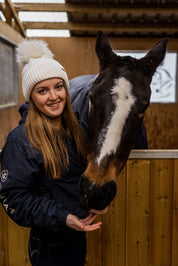 A woman with a horse in the stables wearing the Eva Bobble Hat in Cream