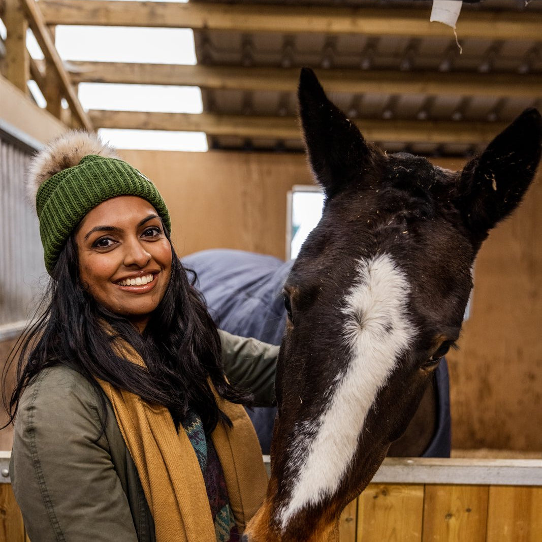A woman with a horse in the stables wearing the Eva Bobble Hat in Forest