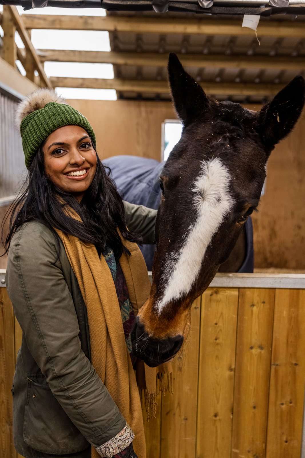 A woman with a horse in the stables wearing the Eva Bobble Hat in Forest