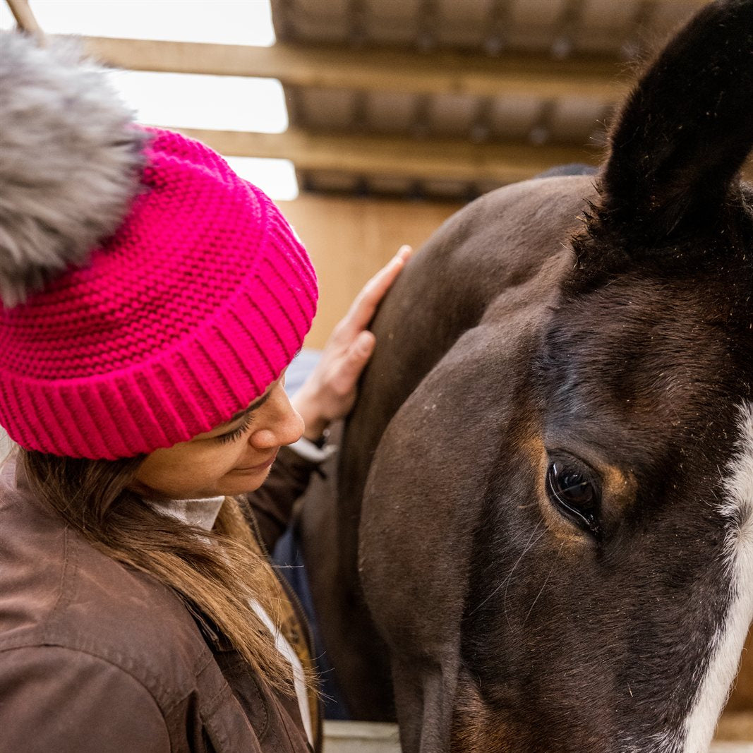 A woman with a horse in the stables wearing the Eva Bobble Hat in Hot Pink
