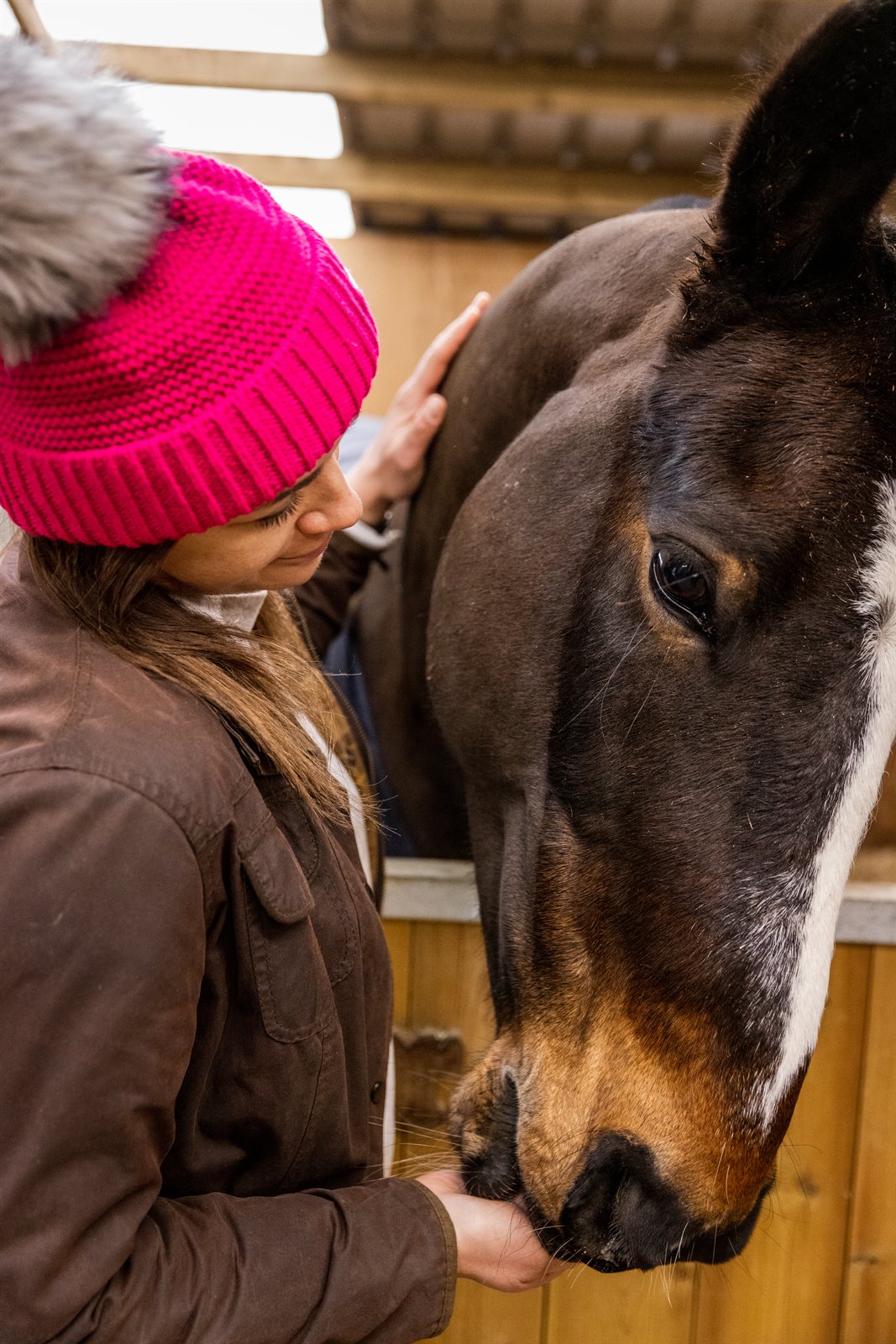 A woman with a horse in the stables wearing the Eva Bobble Hat in Hot Pink