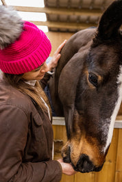 A woman with a horse in the stables wearing the Eva Bobble Hat in Hot Pink