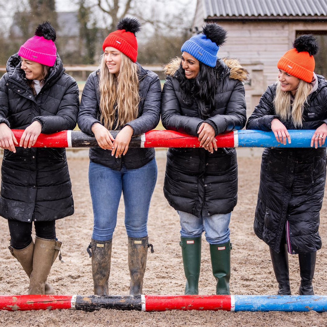 A woman building jumps in a riding arena wearing the Eva Krazi Neon Bobble Hats in all five neon colours