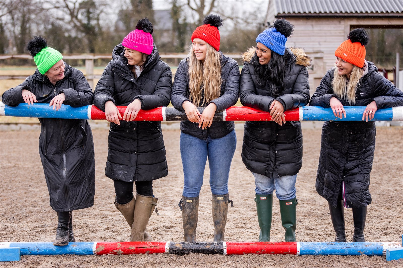 A woman building jumps in a riding arena wearing the Eva Krazi Neon Bobble Hats in all five neon colours