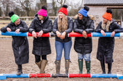 A woman building jumps in a riding arena wearing the Eva Krazi Neon Bobble Hats in all five neon colours