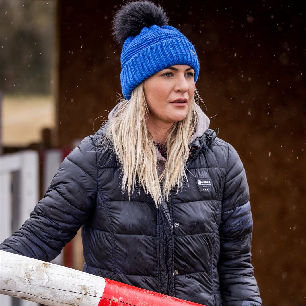 A woman building jumps in a riding arena wearing the Eva Krazi Neon Bobble Hat in Neon Blue
