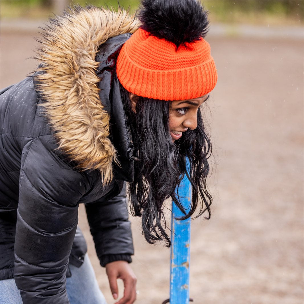 A woman building jumps in a riding arena wearing the Eva Krazi Neon Bobble Hat in Neon Orange