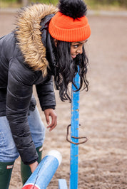 A woman building jumps in a riding arena wearing the Eva Krazi Neon Bobble Hat in Neon Orange