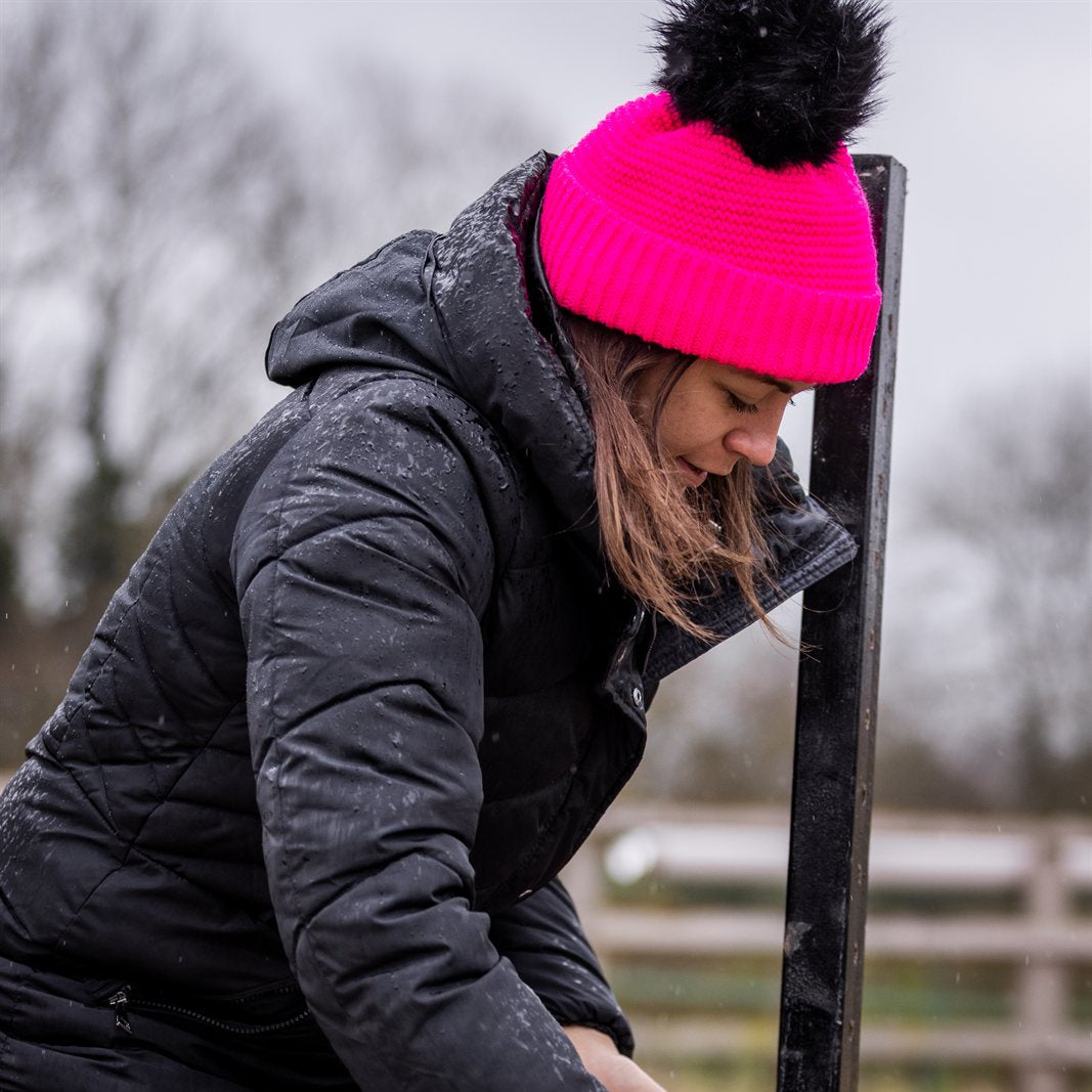 A woman building jumps in a riding arena wearing the Eva Krazi Neon Bobble Hat in Neon Pink