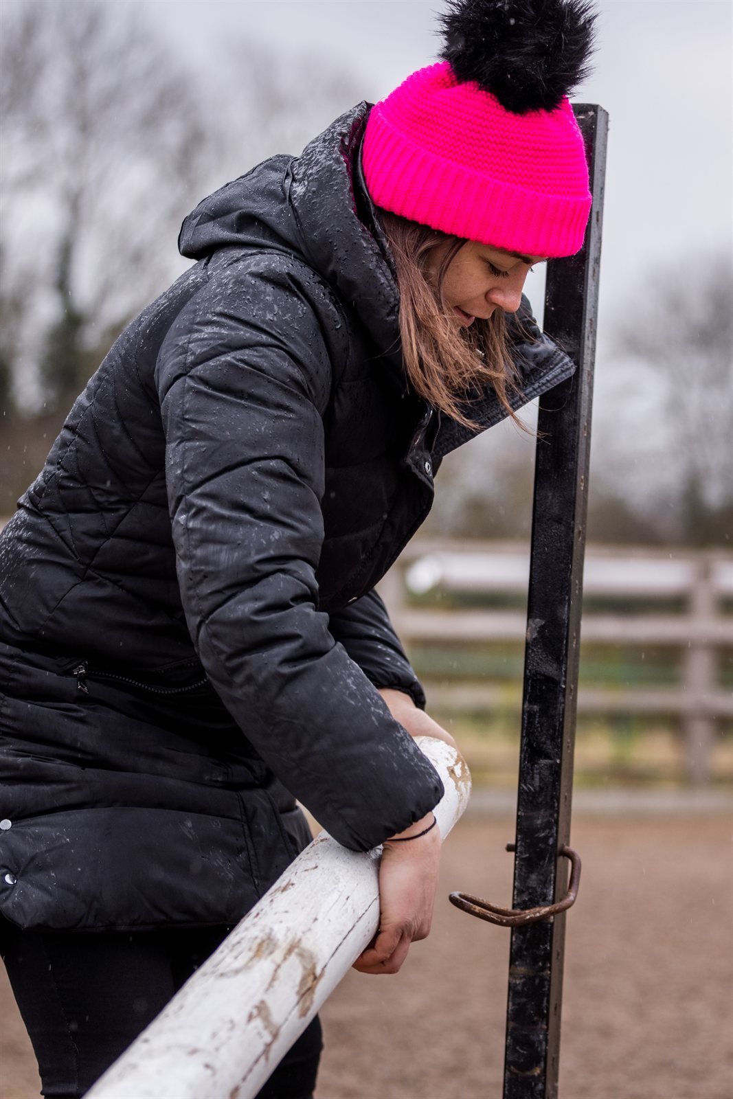A woman building jumps in a riding arena wearing the Eva Krazi Neon Bobble Hat in Neon Pink