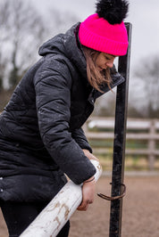 A woman building jumps in a riding arena wearing the Eva Krazi Neon Bobble Hat in Neon Pink