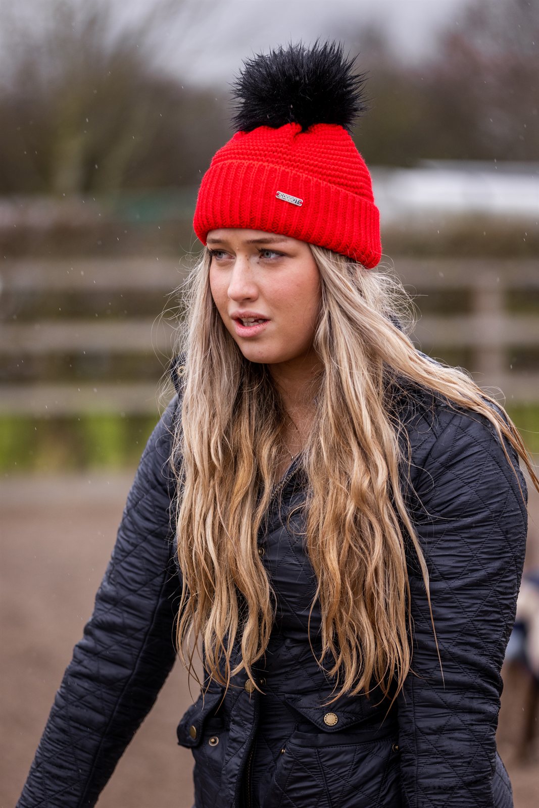 A woman building jumps in a riding arena wearing the Eva Krazi Neon Bobble Hat in Neon Red