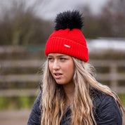 A woman building jumps in a riding arena wearing the Eva Krazi Neon Bobble Hat in Neon Red