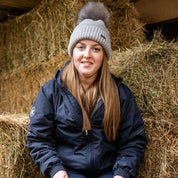 A woman with a horse in the stables wearing the Eva Bobble Hat in Light Grey