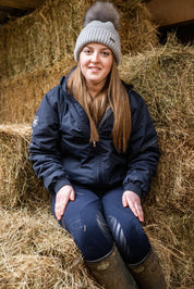 A woman with a horse in the stables wearing the Eva Bobble Hat in Light Grey
