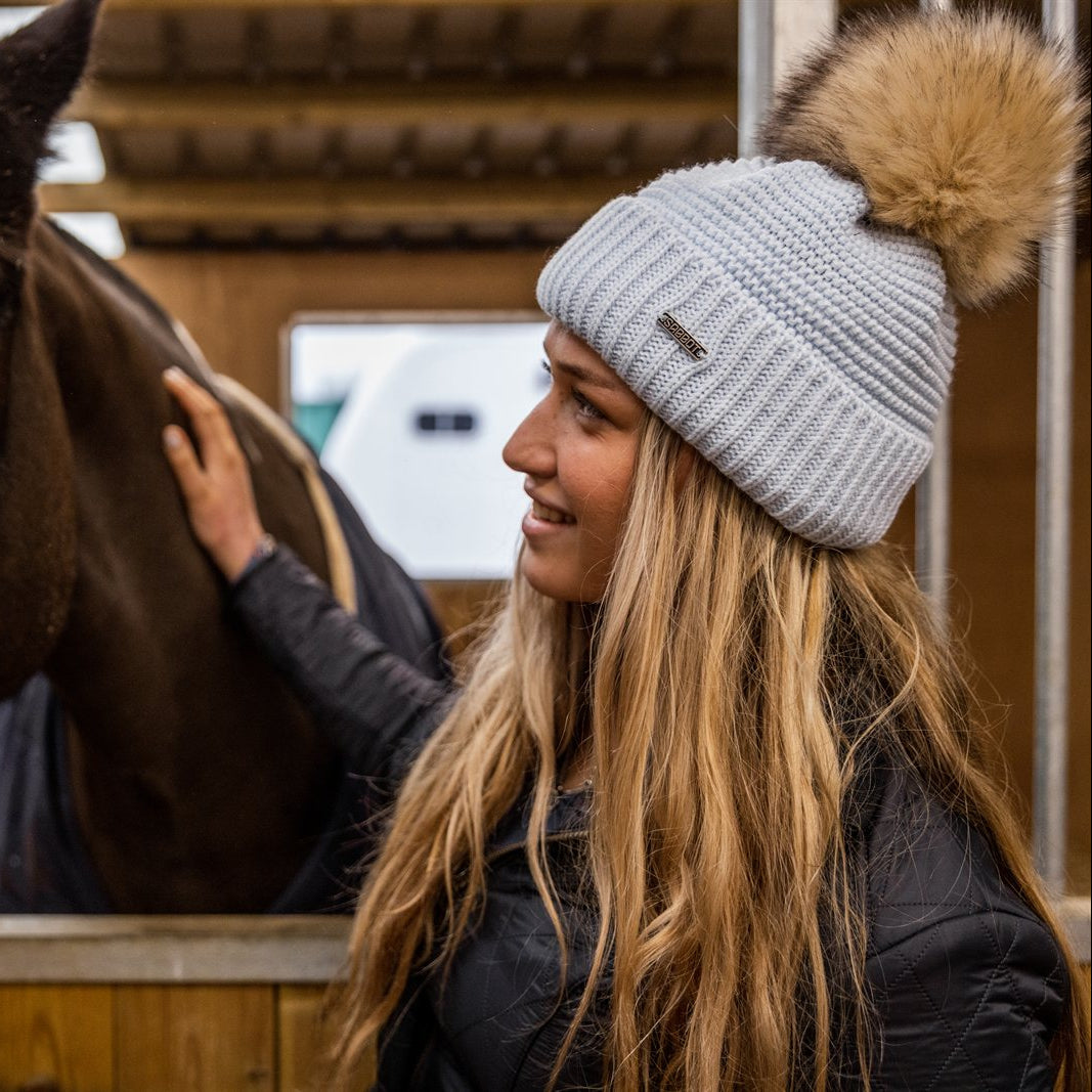 A woman with a horse in the stables wearing the Eva Bobble Hat in Light Grey