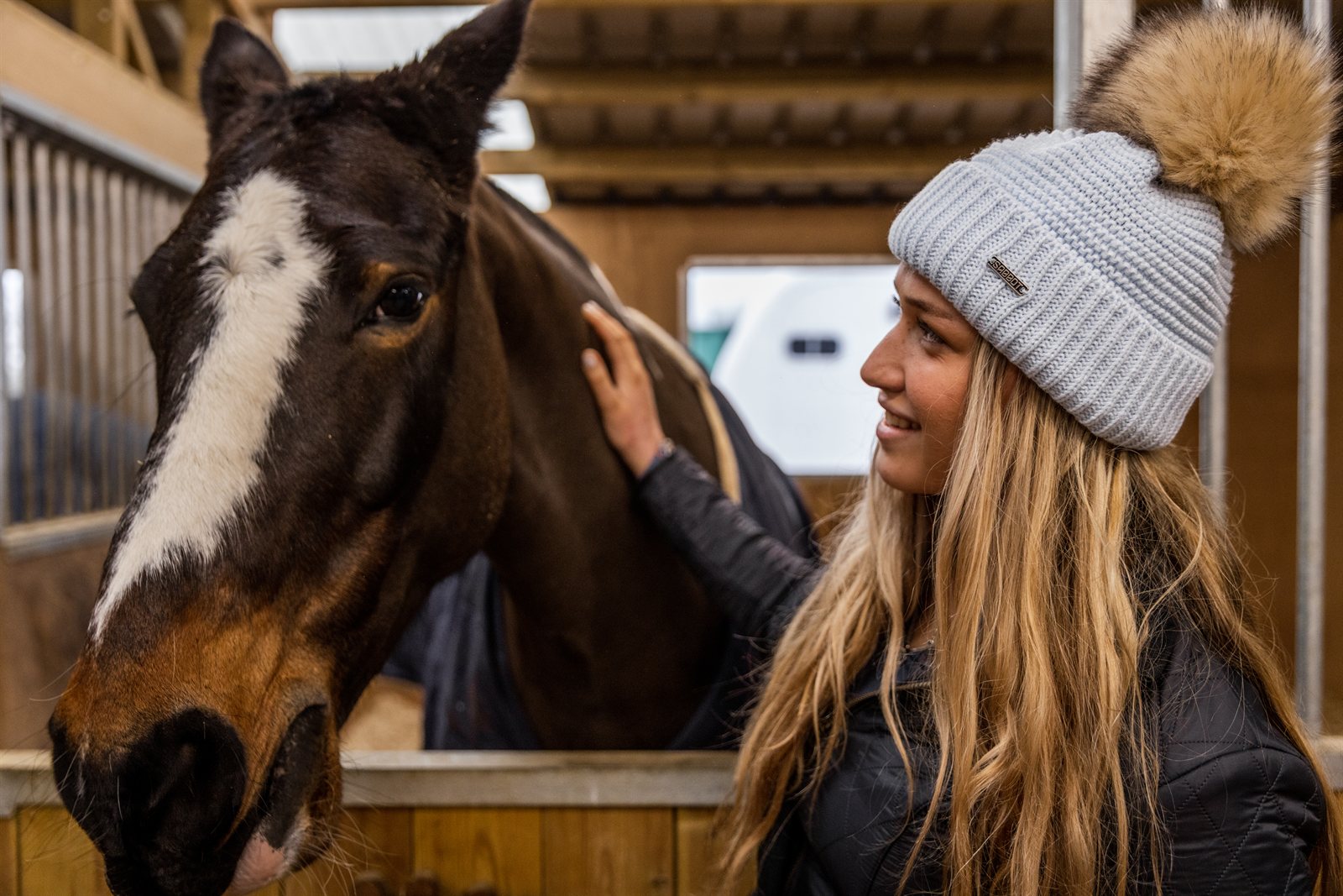A woman with a horse in the stables wearing the Eva Bobble Hat in Light Grey