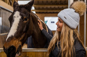 A woman with a horse in the stables wearing the Eva Bobble Hat in Light Grey