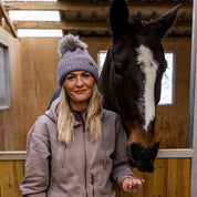 A woman with a horse in the stables wearing the Eva Bobble Hat in Purple