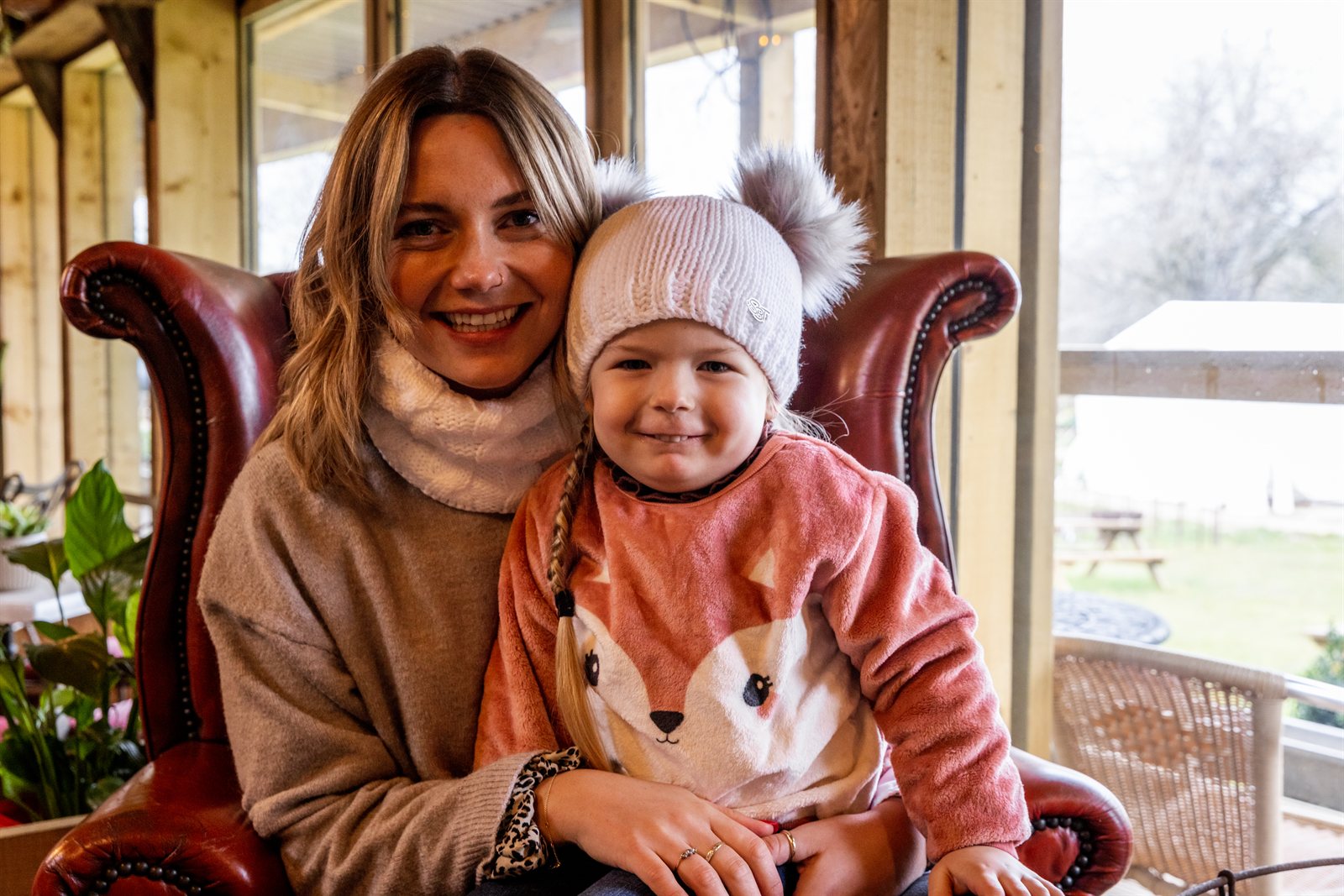 A toddler in a white double pom-pom hat with her mum wearing the Frankie Childrens Bobble Hat in White